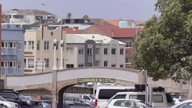 Uma imagem do local do tiroteio que matou 15 pessoas na praia de Bondi, em Sydney, Austrália, mostra uma ponte cinza de 2,7 metros de altura sobre um estacionamento, com prédios ao fundo.
