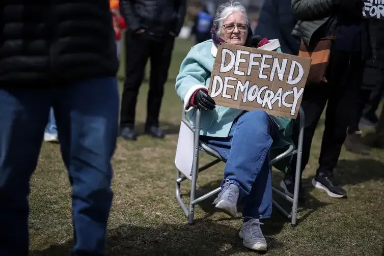 79-year-old Christine Hughes holds a sign as she attends a demonstration during the day of 